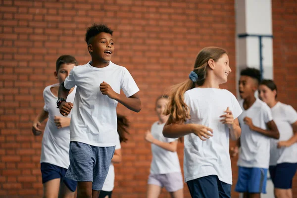 Multi-ethnic group of school children running on PE class at school gym. Focus is on African American boy. 