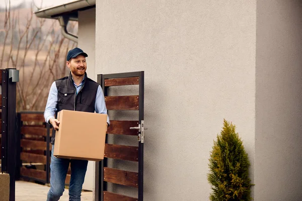 Smiling Male Courier Carrying Cardboard Box While Making Home Delivery — Stockfoto