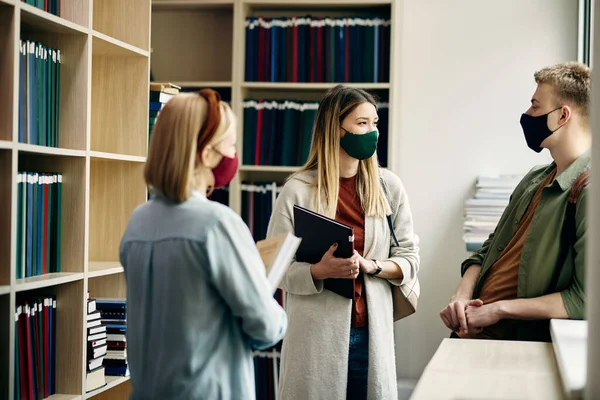 Group of college students communicating while wearing protective face masks and learning in library.