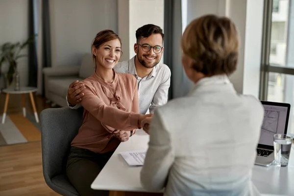 Young happy couple shaking hands with insurance agent during a meeting in the office. 