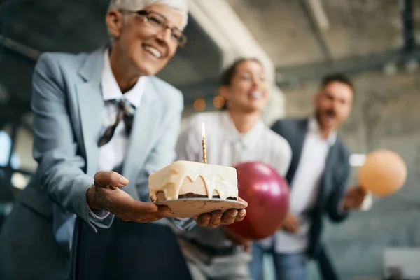 Close-up of mature businesswoman holding a cake while celebrating Women\'s day  with coworkers in the office.