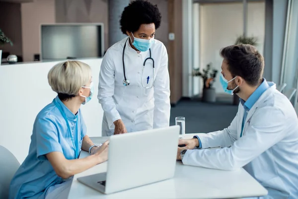 Black female doctor and her colleagues wearing protective face masks and communicating while working in the hospital.