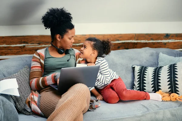 African American working mother using laptop and communicating with her daughter at home.