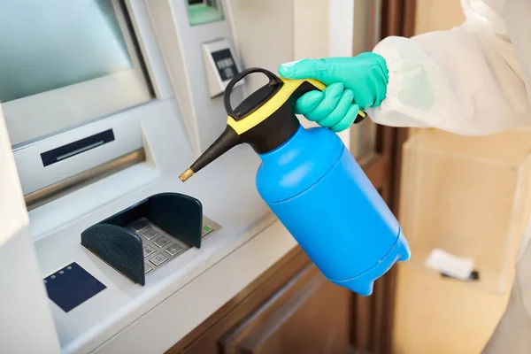 Close-up of sanitation worker doing disinfection of ATM in the city due to COVID-19 epidemic.