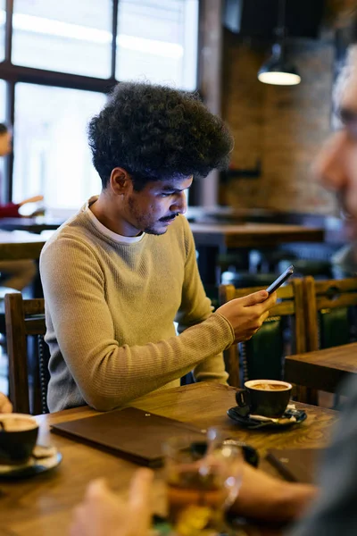 Young Lebanese man using cell phone and reading text message while drinking coffee with friends in a cafe.