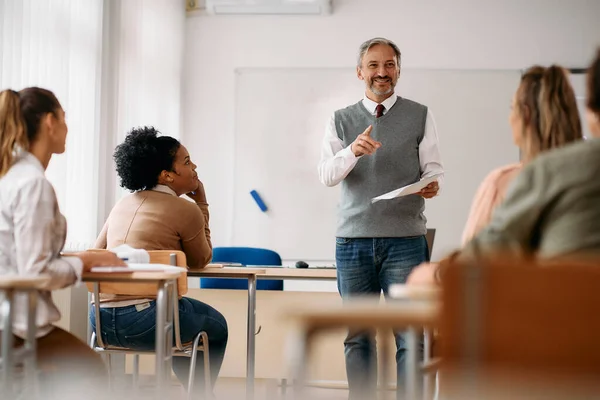 Happy mature teacher talking to group of his students during a class at lecture hall.