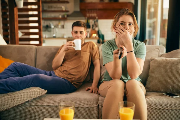 Bored woman changing channels while watching TV with her boyfriend in the living room.