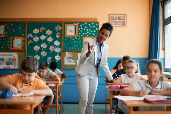 Black elementary school teacher assisting her students during class in the classroom.