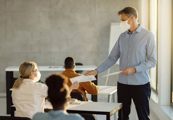 University students getting test results from their professor while wearing protective face masks due to coronavirus epidemic. Focus is on professor.