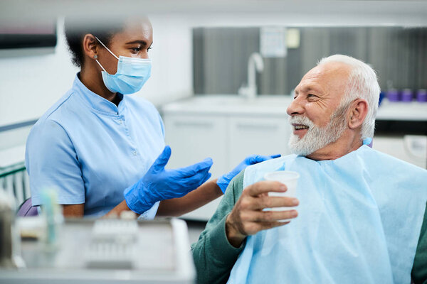 African American dental nurse communicating with senior patient during dental procedure at dentist's office. 
