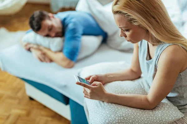 Young Worried Woman Using Smart Phone While Her Boyfriend Napping — Foto de Stock