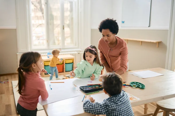 African American preschool teacher and group of creative kids drawing on art class.