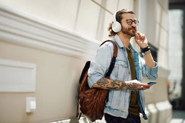 University student enjoying in music over headphones with eyes closed while using mobile phone in a hallway. Copy space.