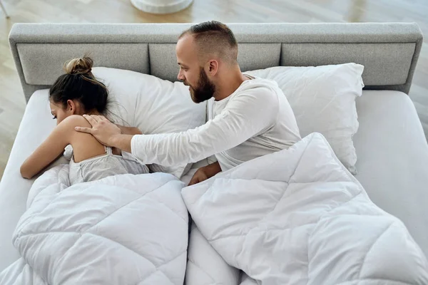 High angle view of a man trying to talk with his displeased girlfriend who is ignoring him in the bedroom. 