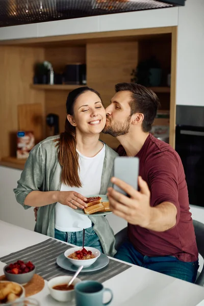 Young Man Kissing His Wife Using Using Smart Phone Kissing — Stockfoto