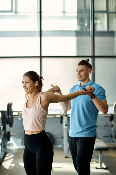 Smiling  sportswoman doing stretching exercise with assistance of her personal trainer in a gym.