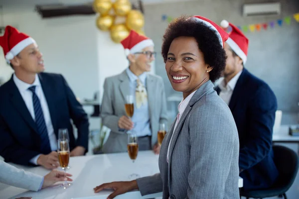 Happy black businesswoman and her coworkers having New Year\'s party in the office. She is looking at the camera.