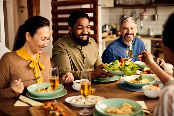 Group of happy people having dinner at home. Focus is on black man passing salad to his friend.