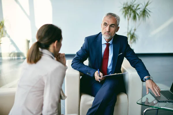 Senior psychiatrist using laptop during individual therapy with female patient at psychotherapy center.