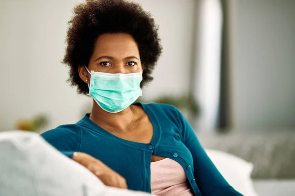 Black woman wearing face mask while relaxing on the sofa and thinking of something.