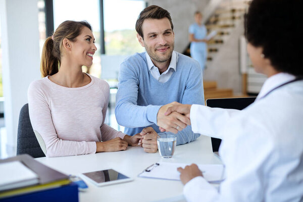 Счастливый мужчина рукопожатия с врачом, находясь со своей женой в медицинской клинике. 