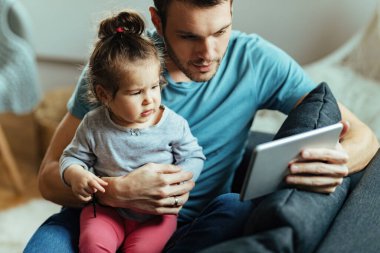 Mutlu baba ve küçük kızı evde dinlenirken dokunmatik ekranda çizgi film izliyorlar.. 
