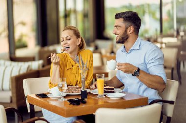 Happy woman enjoying in dessert while her boyfriend is drinking coffee in a cafe. 