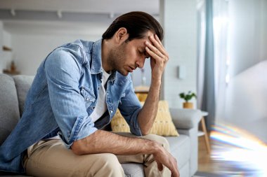 Young man having a headache and holding his head in pain at home. 
