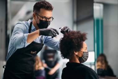African American woman having a haircut at hairdresser's during coronavirus pandemic. Focus is on hairdresser. 