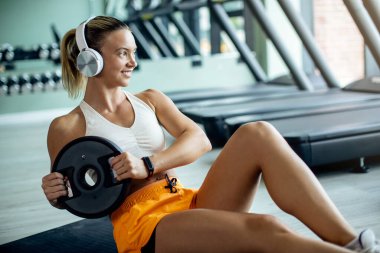 Smiling athletic woman exercising sit-ups with weight plate at health club. 