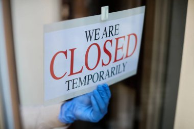 Close-up of waitress hanging closed sign at entrance door of a cafe during COVID-19 epidemic. 