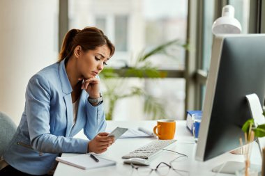 Young sad businesswoman using cell phone and reading text message while working in the office. 