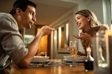 Low angle view of young happy couple having dinner and talking to each other in dining room. 