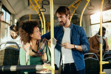 Happy African American woman talking to her male friend while traveling by bus. 