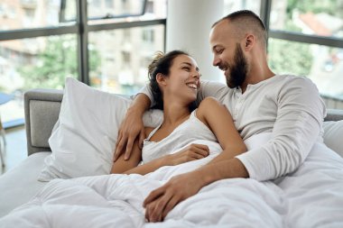 Happy couple communicating while lying embraced on in the bedroom. 
