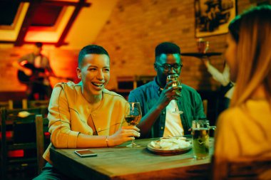 Young black woman and her friends having fun while communicating on their night out in a pub.