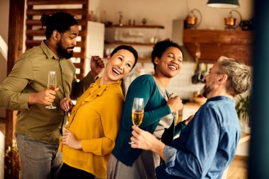 Happy diverse group of friends drinking wine while having fun and dancing at home. 