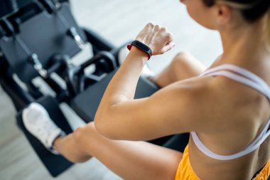 Close-up of sportswoman using fitness tracker while working out on exercise machine in a gym.