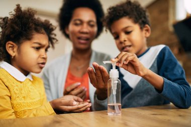 Close-up of African American family using hand sanitizer at home. 