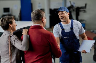 Happy auto repairman shaking hands with his customers in a workshop. 