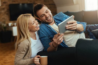 Young happy couple having fun while using digital tablet at home. 