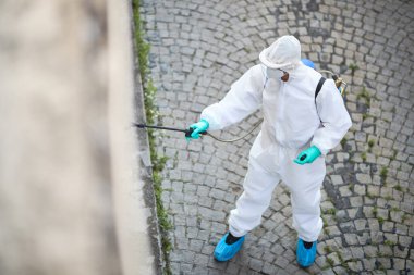 High angle view of sanitation worker in protective suit spraying city streets with disinfectant during COVID-19 epidemic. Copy space. 