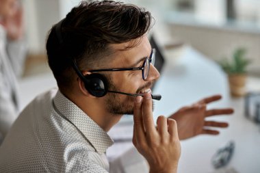 Happy call center agent wearing headset while talking with clients and working in the office. 