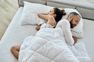 High angle view of young couple lying back to back while having relationship  problems in bedroom. 