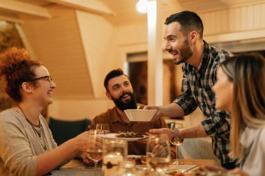 Small group of young happy adults having fun while eating dinner at dining table at home.