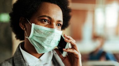 Close-up of African American businesswoman wearing face mask for virus protection while talking on the phone at the airport. 