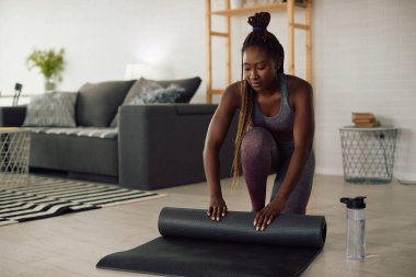Genç Afrikalı Amerikalı atletik kadın oturma odasında egzersiz minderini açıyor.. 