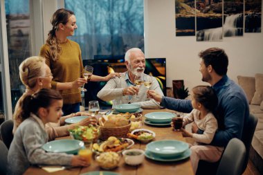 Happy senior man toasting with his extended family during a meal at dining table.