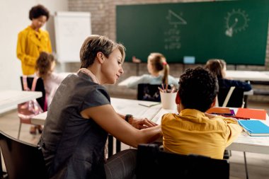 Female teacher helping elementary student with studying in the classroom. 