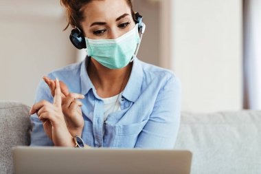Young smiling woman wearing protective mask on her face while having video call on a computer at home. 